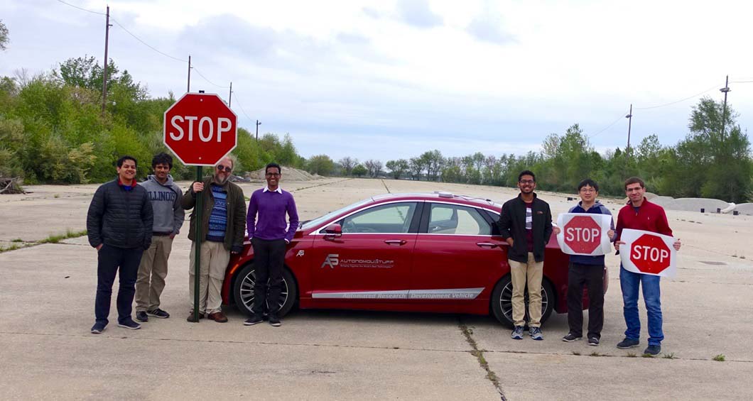 People standing next to a red car and holding stop signs